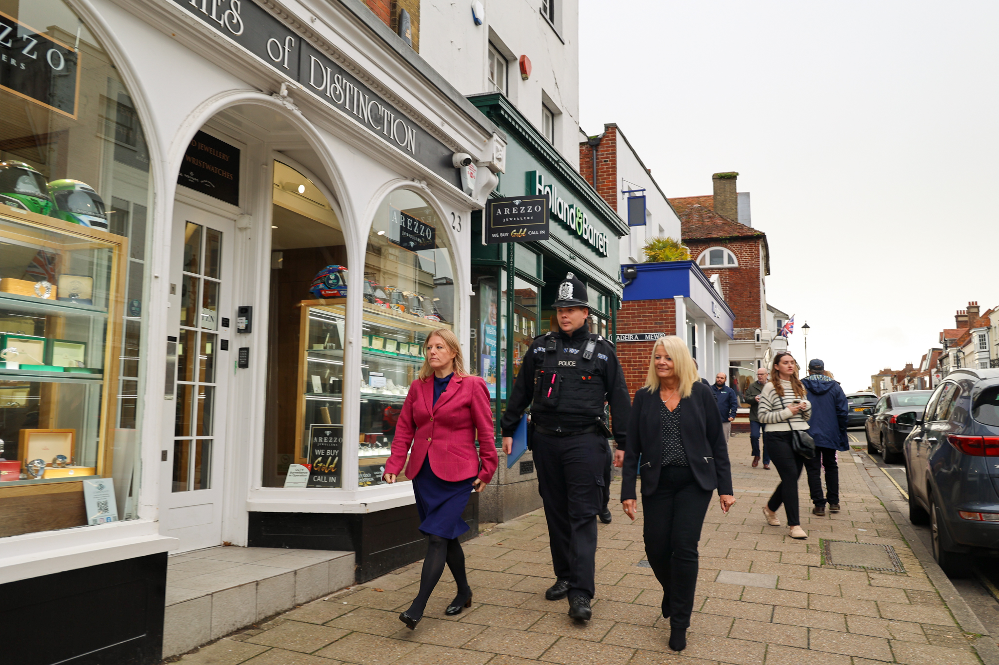 The Police and Crime Commissioner, a police officer and a local authority representative walk together along Lymington High Street. Shops, signage and pedestrians appear in the background as they continue their visit to local businesses.